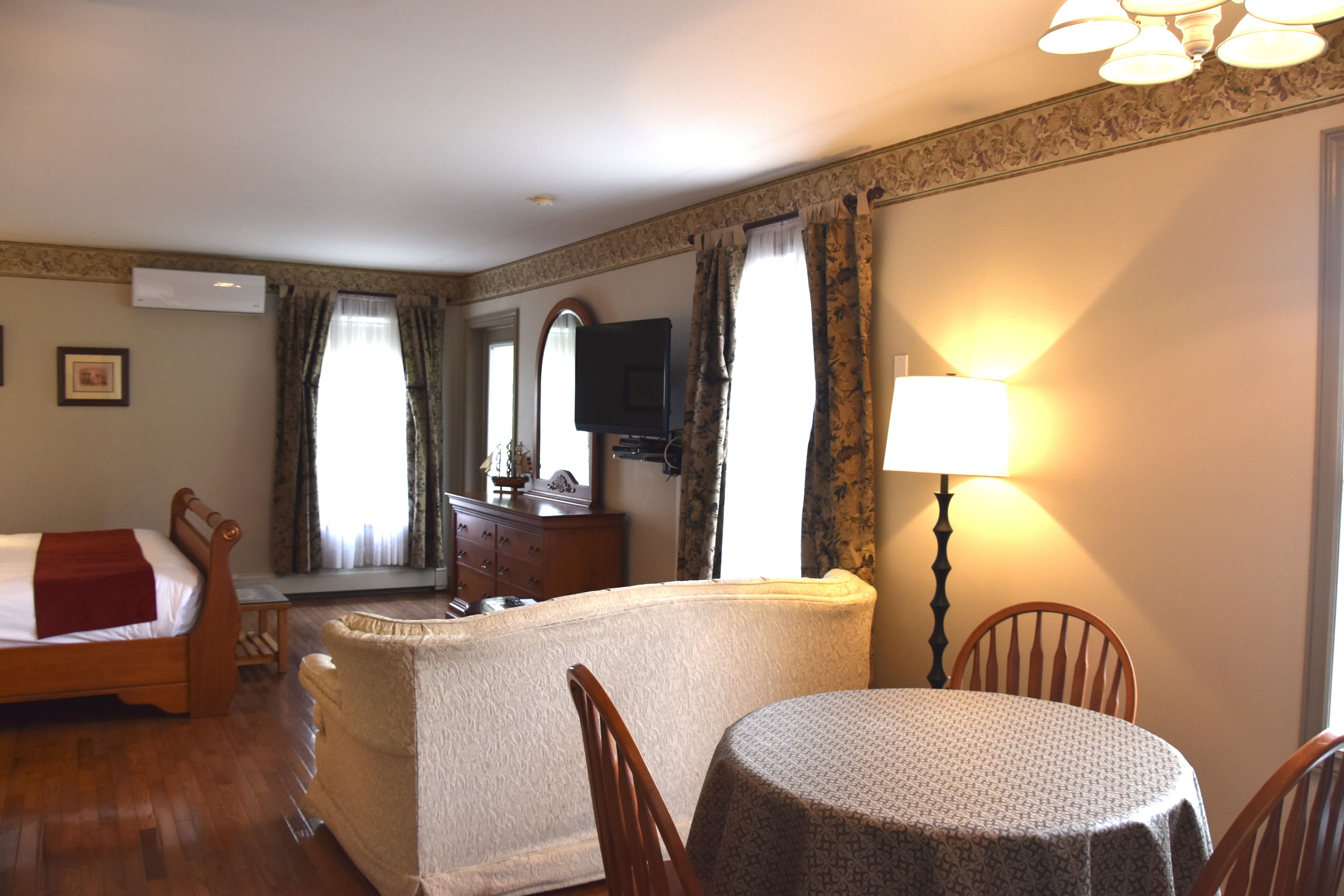 Habitación de hotel con cama, sofá, mesa de comedor, lámpara, televisión y cómoda.