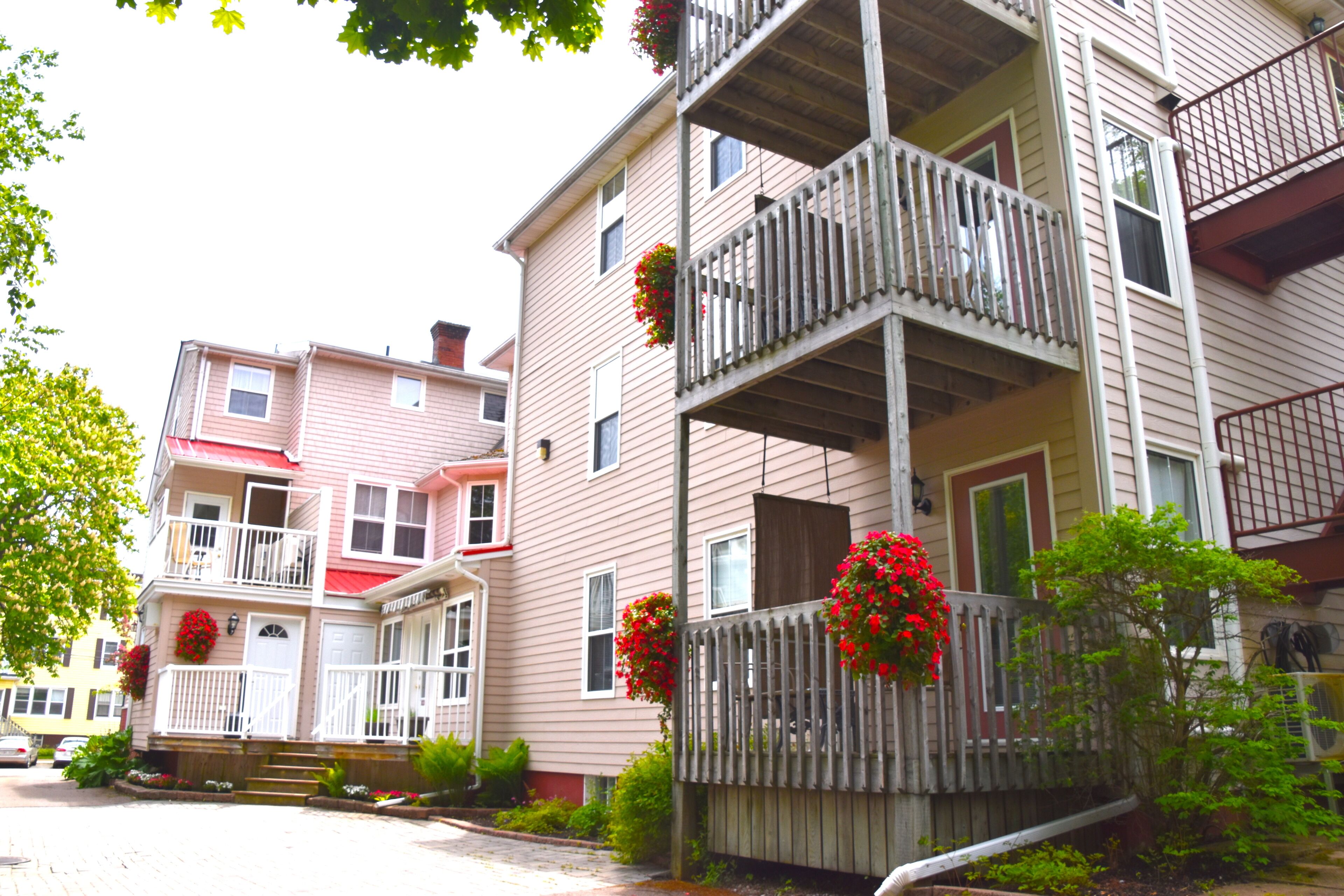 A multi-story residential building with a balcony on the second floor, a front porch with steps, and a wooden fence.
