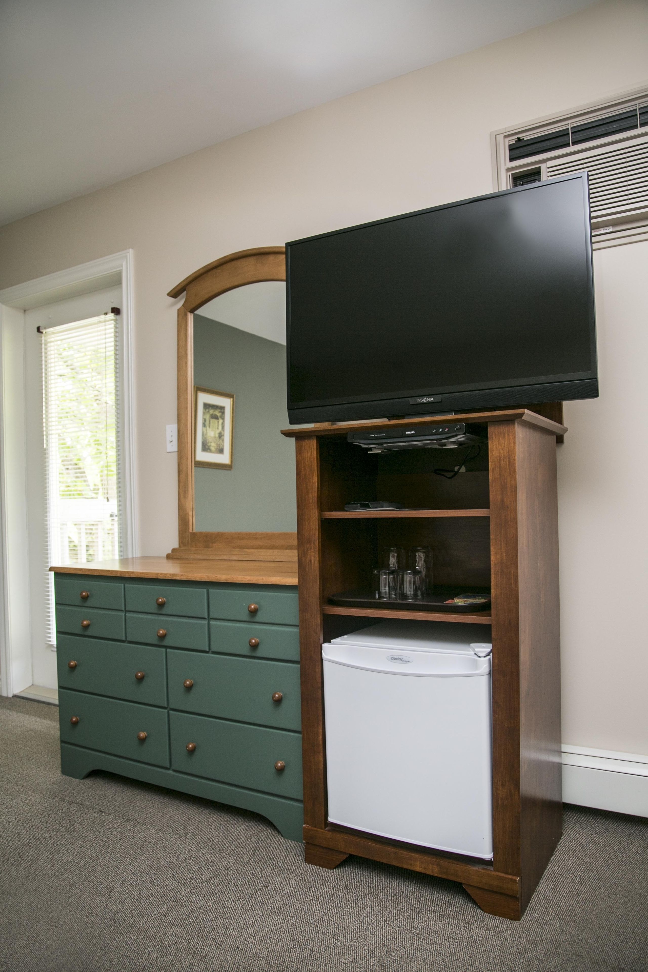 Een kamer met een houten dressoir, een televisie erboven en een witte koelkast.