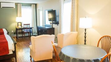 A hotel room with a bed, a desk, a chair, a table, a TV, and a lamp.