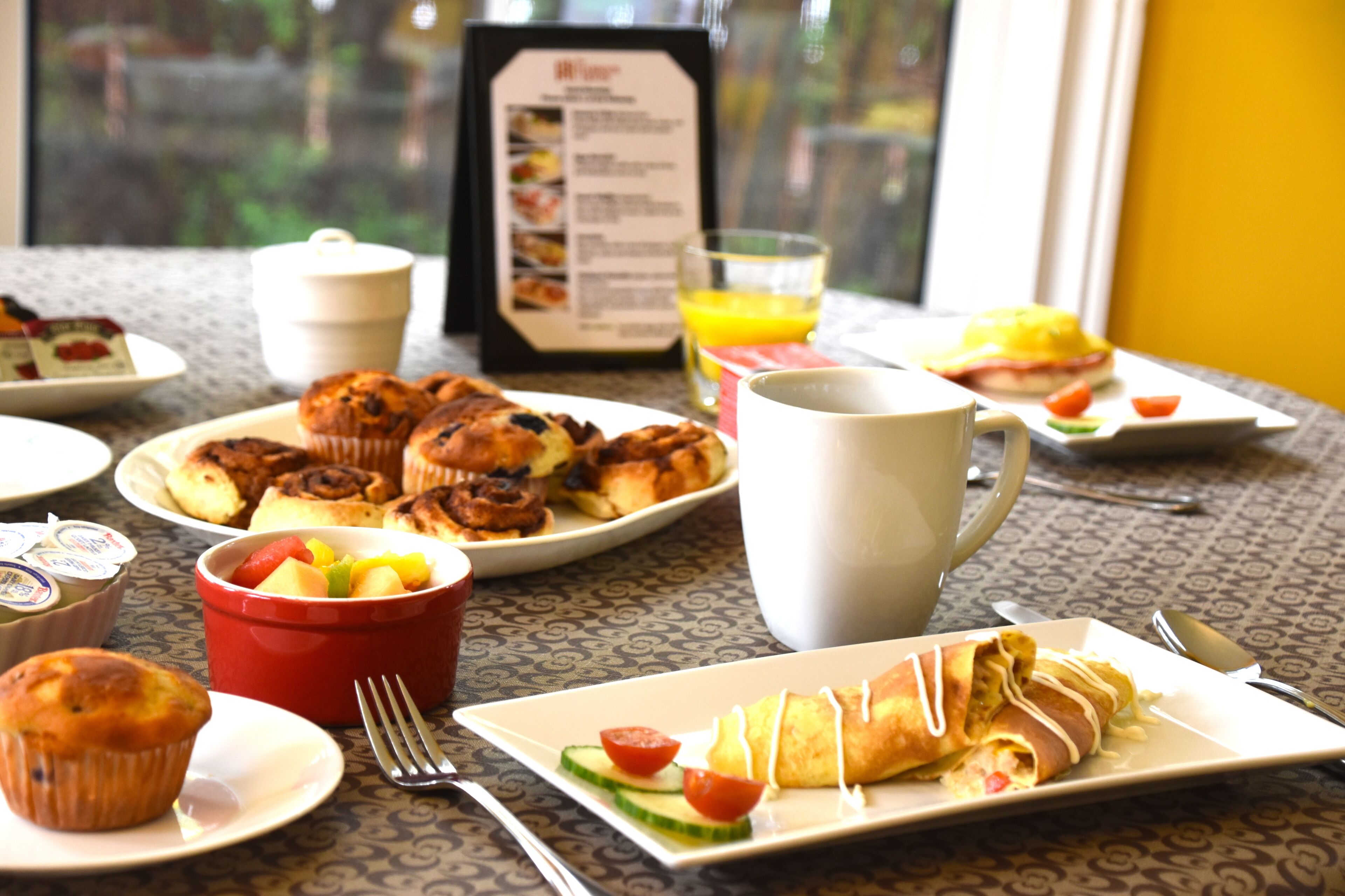 A breakfast table with various dishes, a menu, and a cup of coffee.