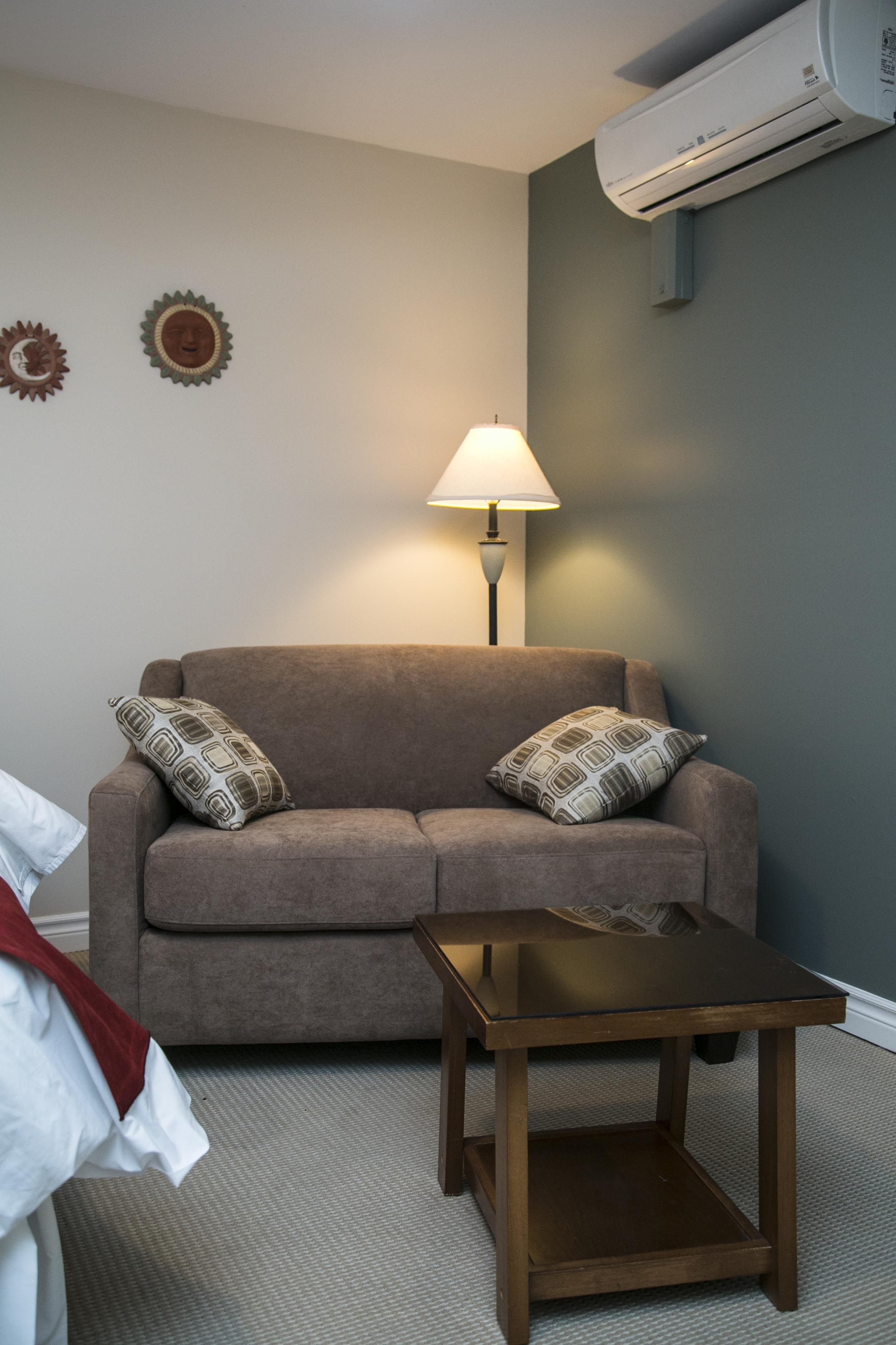 A living room with a sofa, two patterned pillows, a table, a lamp, and an air conditioning unit.