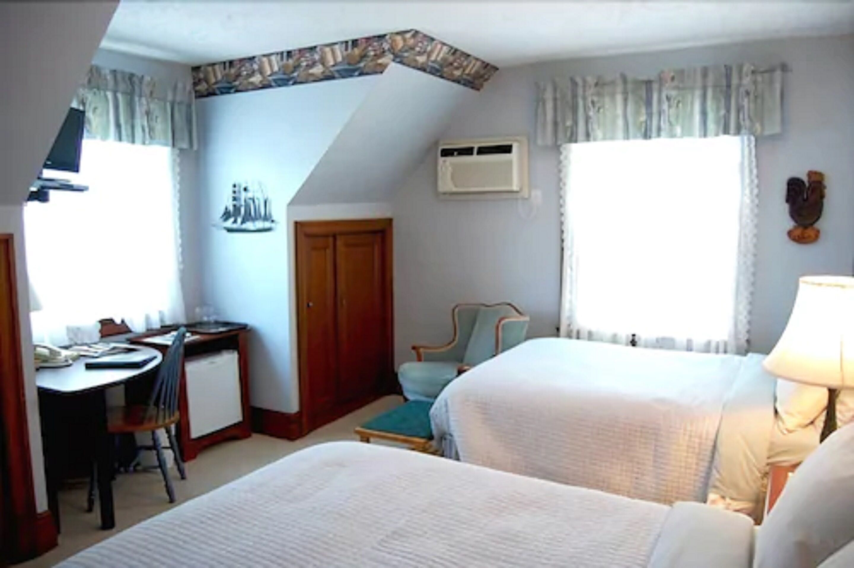 A hotel room with two beds, a desk, a chair, and a window with curtains.