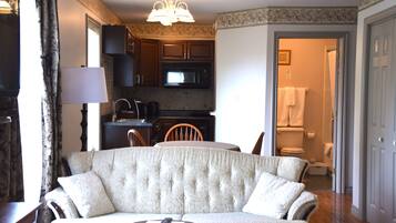 Ein Wohnzimmer mit Sofa, Couchtisch und Fernseher. Eine Küchenzeile mit Mikrowelle und Schränken ist vorhanden. Ein Badezimmer ist durch eine offene Tür zu sehen.