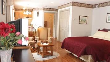 A bedroom with a bed, a chair, a table, and a TV.
