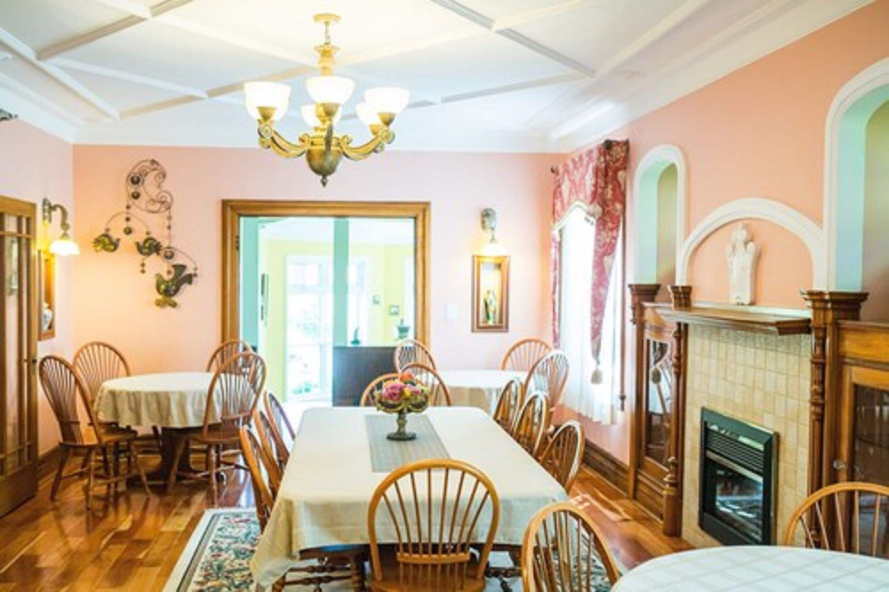 A dining room with a long table, wooden chairs, a chandelier, and a fireplace.