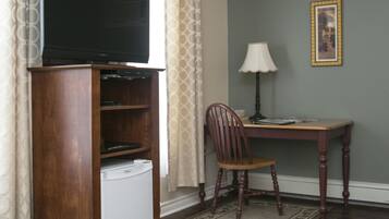 Een kamer met een houten tv-meubel, een bureau met een lamp, een stoel en een lijst met een afbeelding aan de muur.