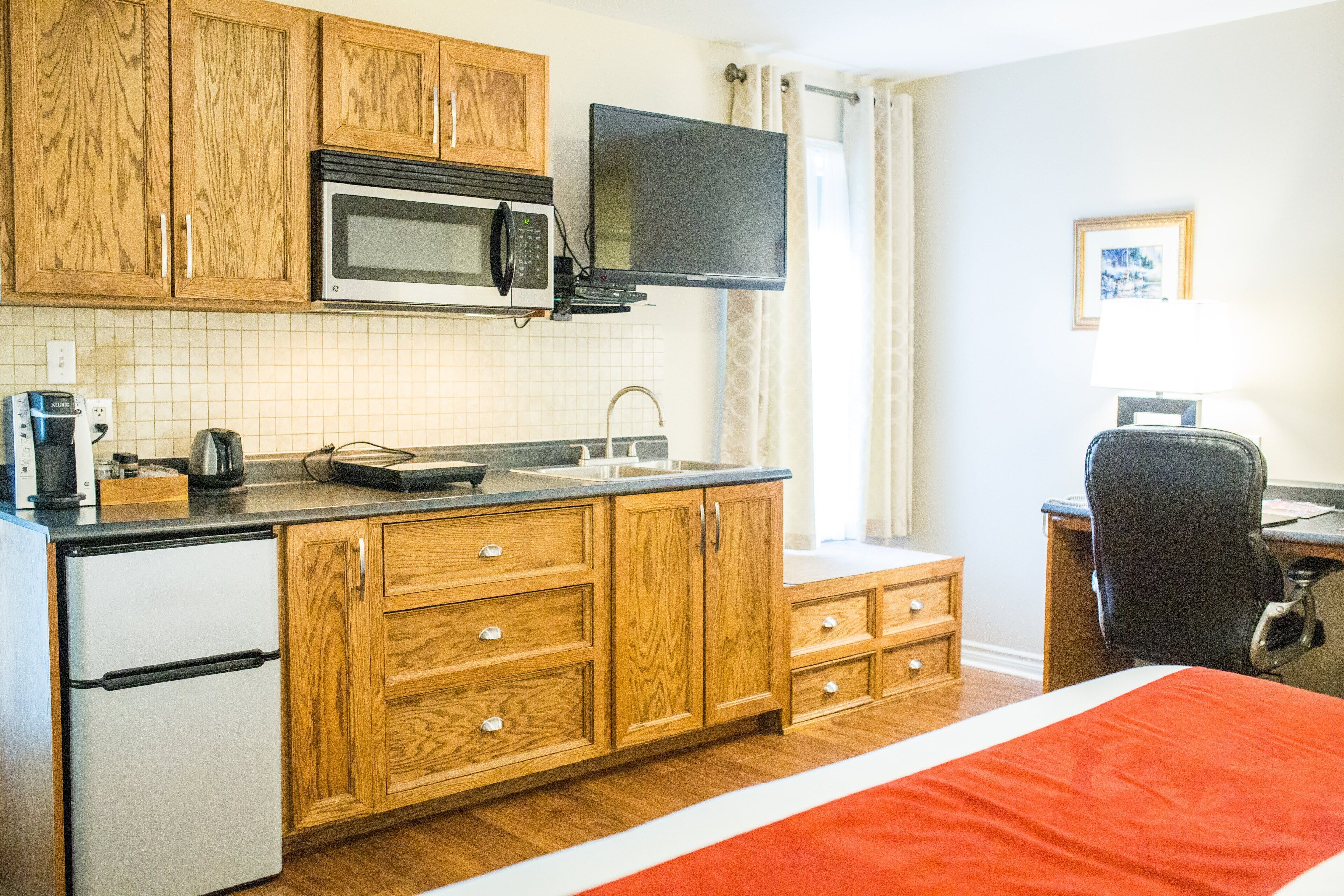 A compact kitchen with wooden cabinets, a microwave, a coffee maker, and a small refrigerator.