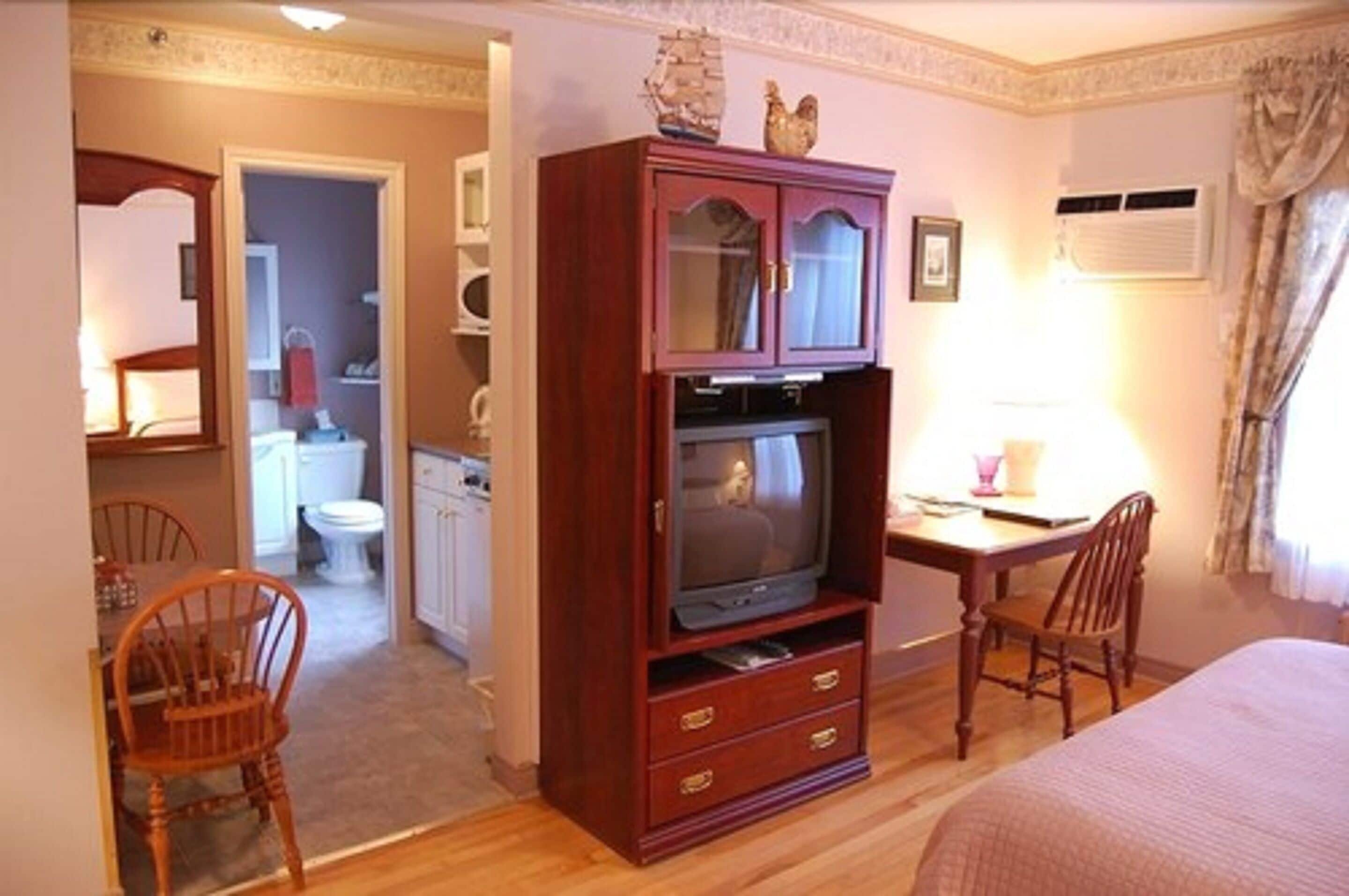 Una habitación de hotel con un armario de madera, un televisor, un escritorio con una silla y una cama.