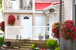 A two-story house with a white front door, a balcony with white railings, and red flowers in hanging planters. - The Harbour House (Charlottetown)