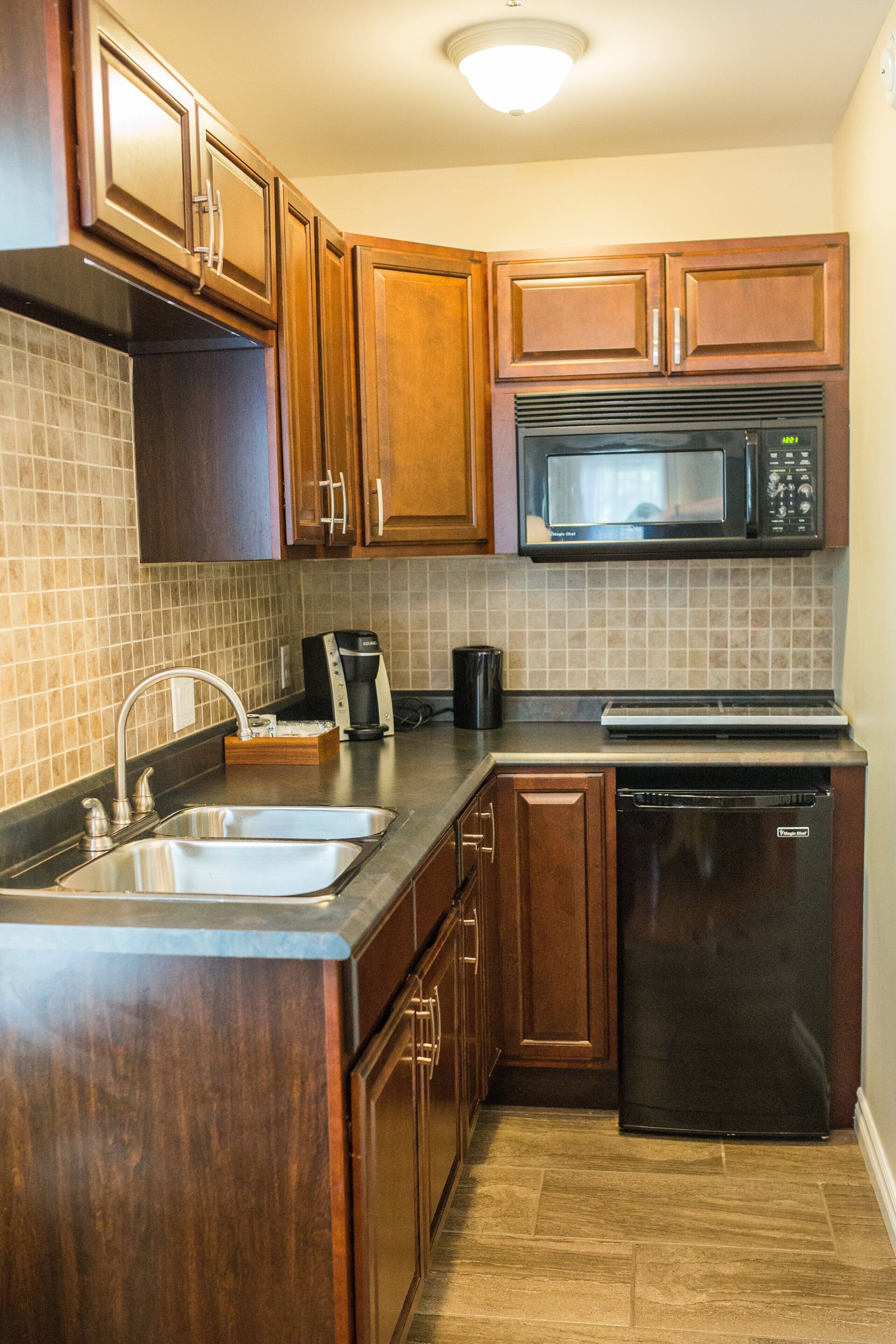 A kitchen with wooden cabinets, a stainless steel sink, a microwave, a coffee maker, and a dishwasher.