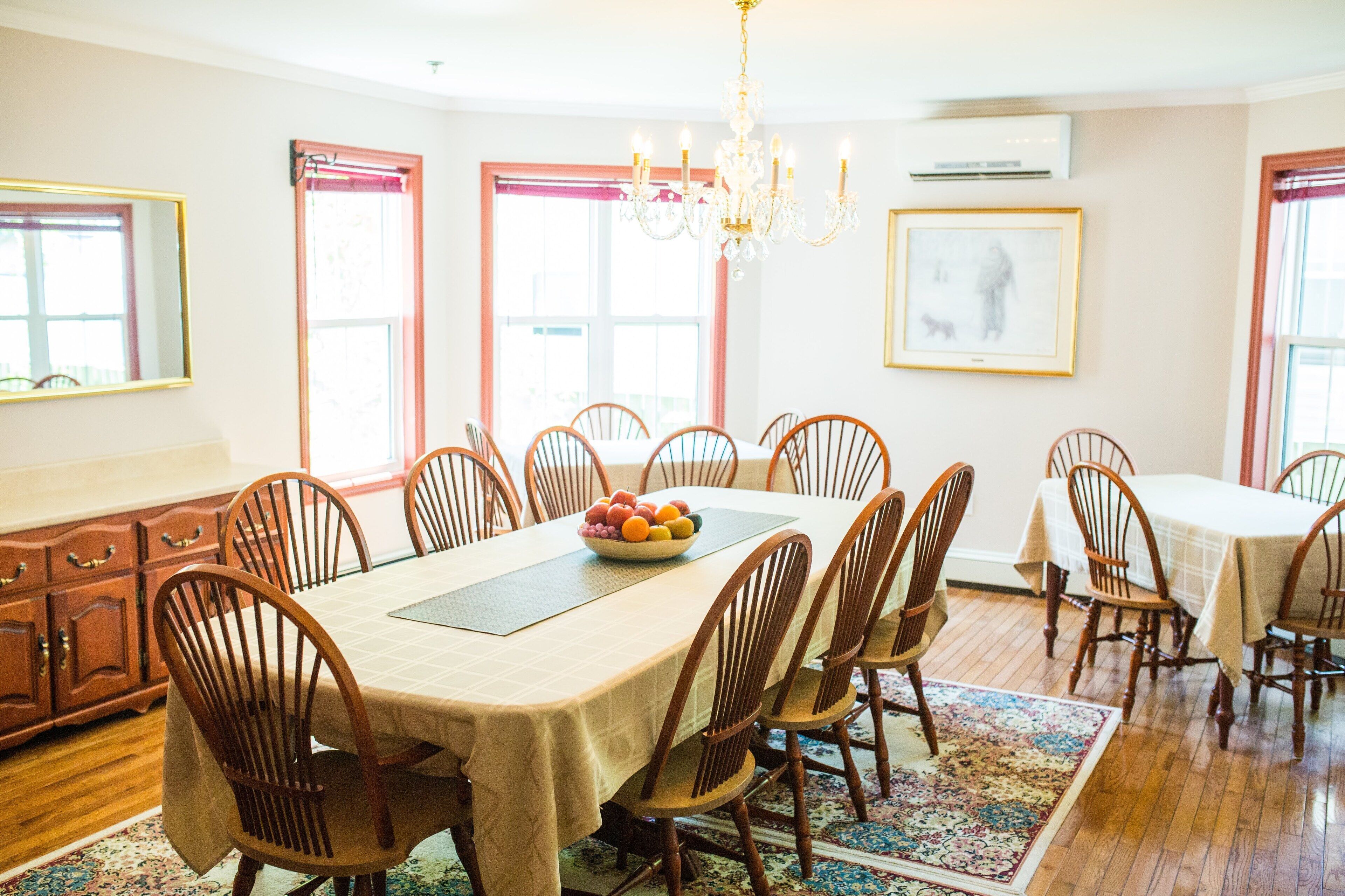 Une salle à manger avec une grande table, des chaises en bois, un lustre et un panier de fruits.