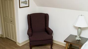 A room with a wooden floor, a brown armchair, a small table with a lamp, a framed picture on the wall, and a door.