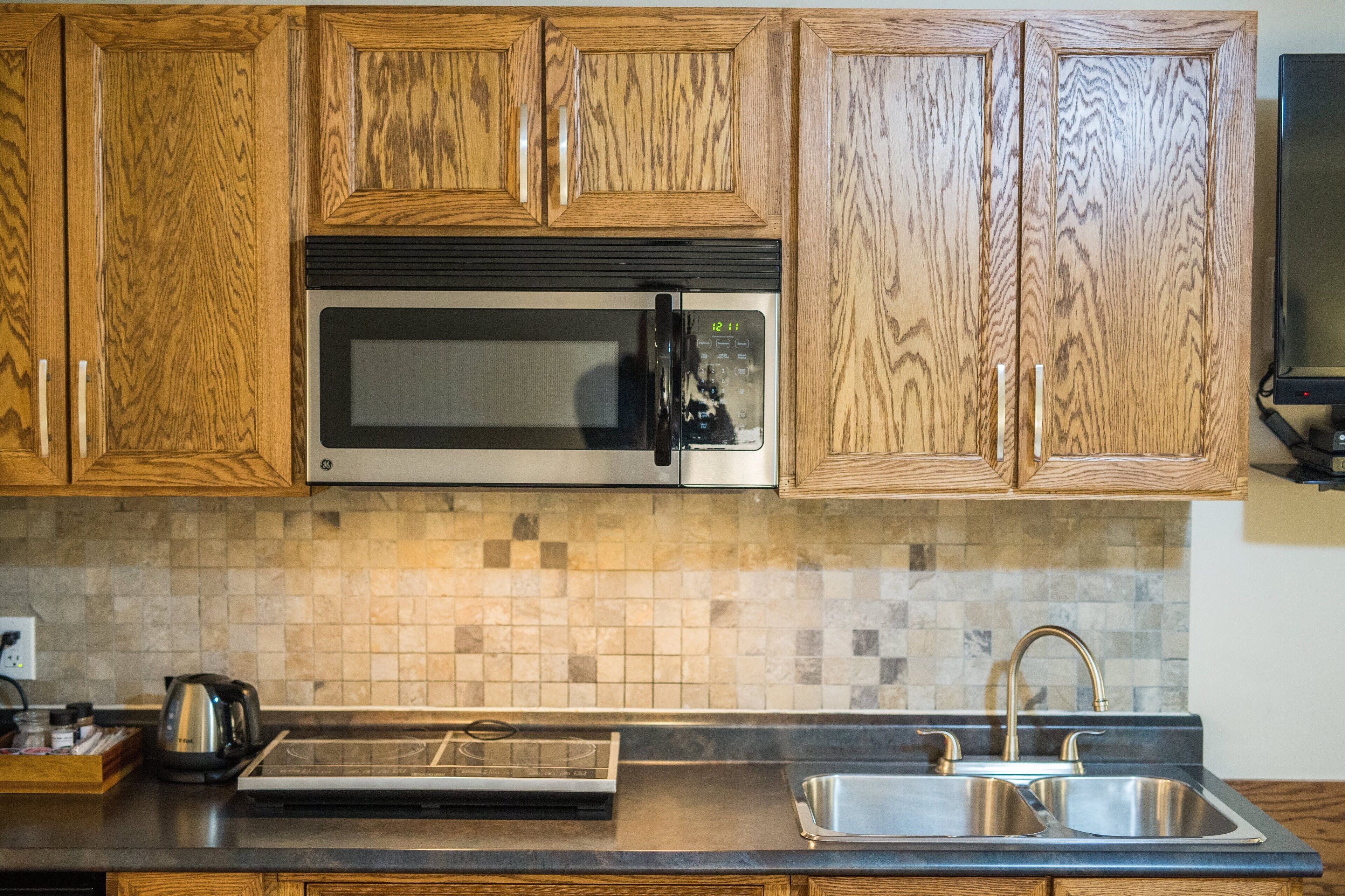 A kitchen with wooden cabinets, a stainless steel microwave, a built-in stove, and a double sink.