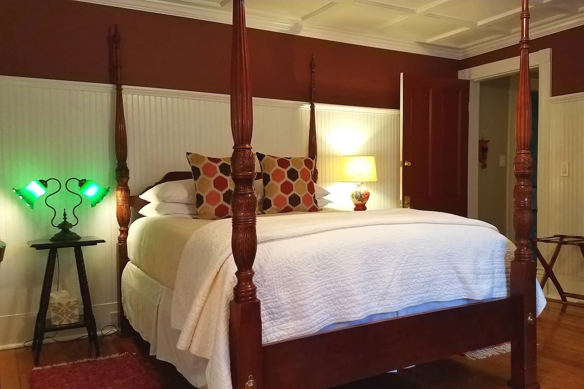 A four-poster bed with a white quilt, a bedside table with a lamp, and a wooden dresser.