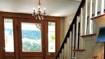 A spacious room with a wooden floor, a large wooden dining table, a chandelier, and a staircase with a 'Happy Holiday' sign.