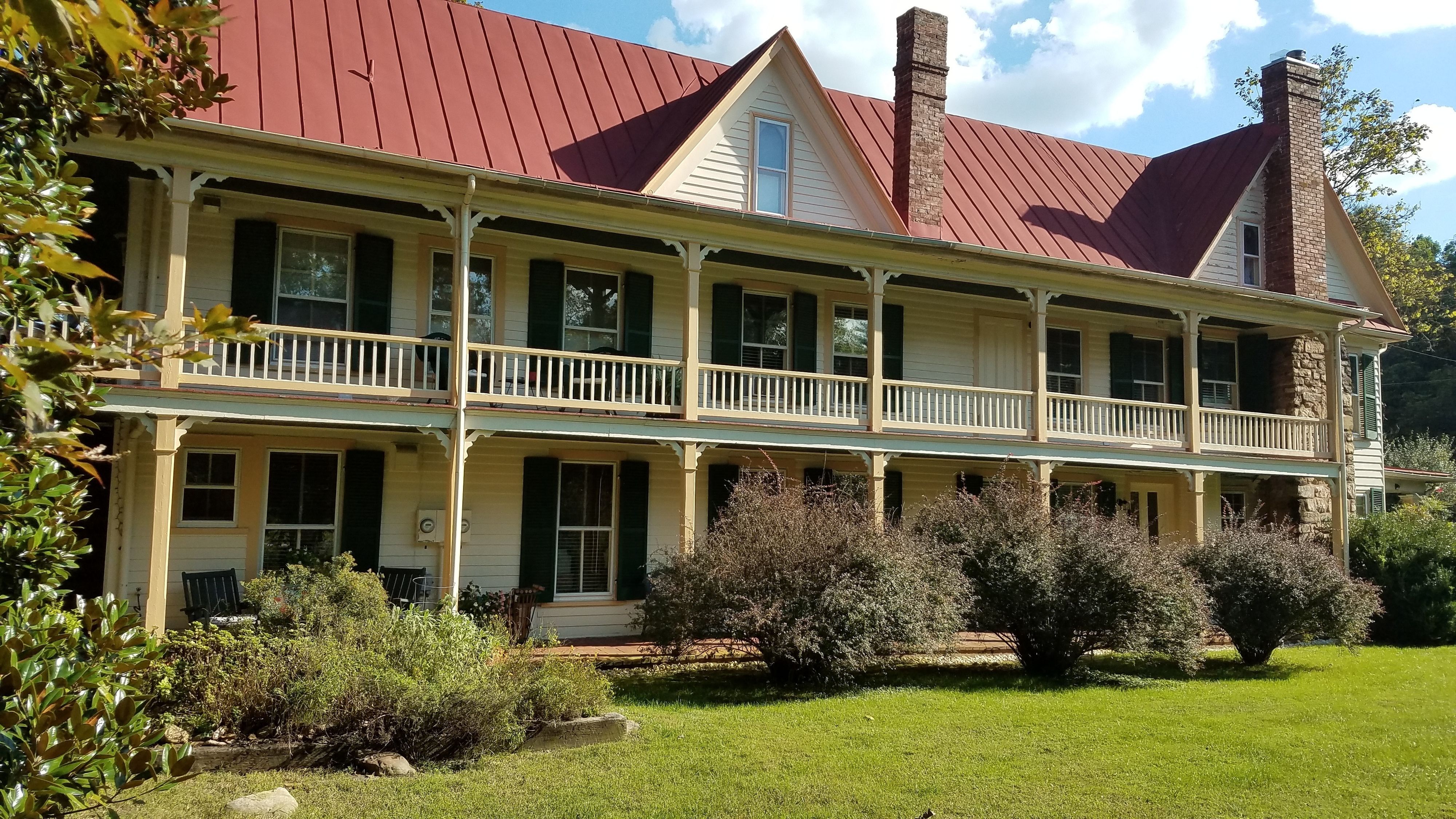 A two-story house with a red roof, a balcony on the second floor, and a well-maintained lawn.