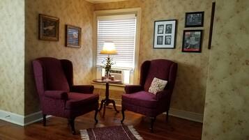 Una habitación con dos sillones morados, una mesita con lámpara y una ventana con persianas.