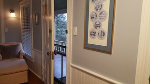 A hallway with a door leading to a balcony, a framed picture on the wall, and a chair with a cushion.