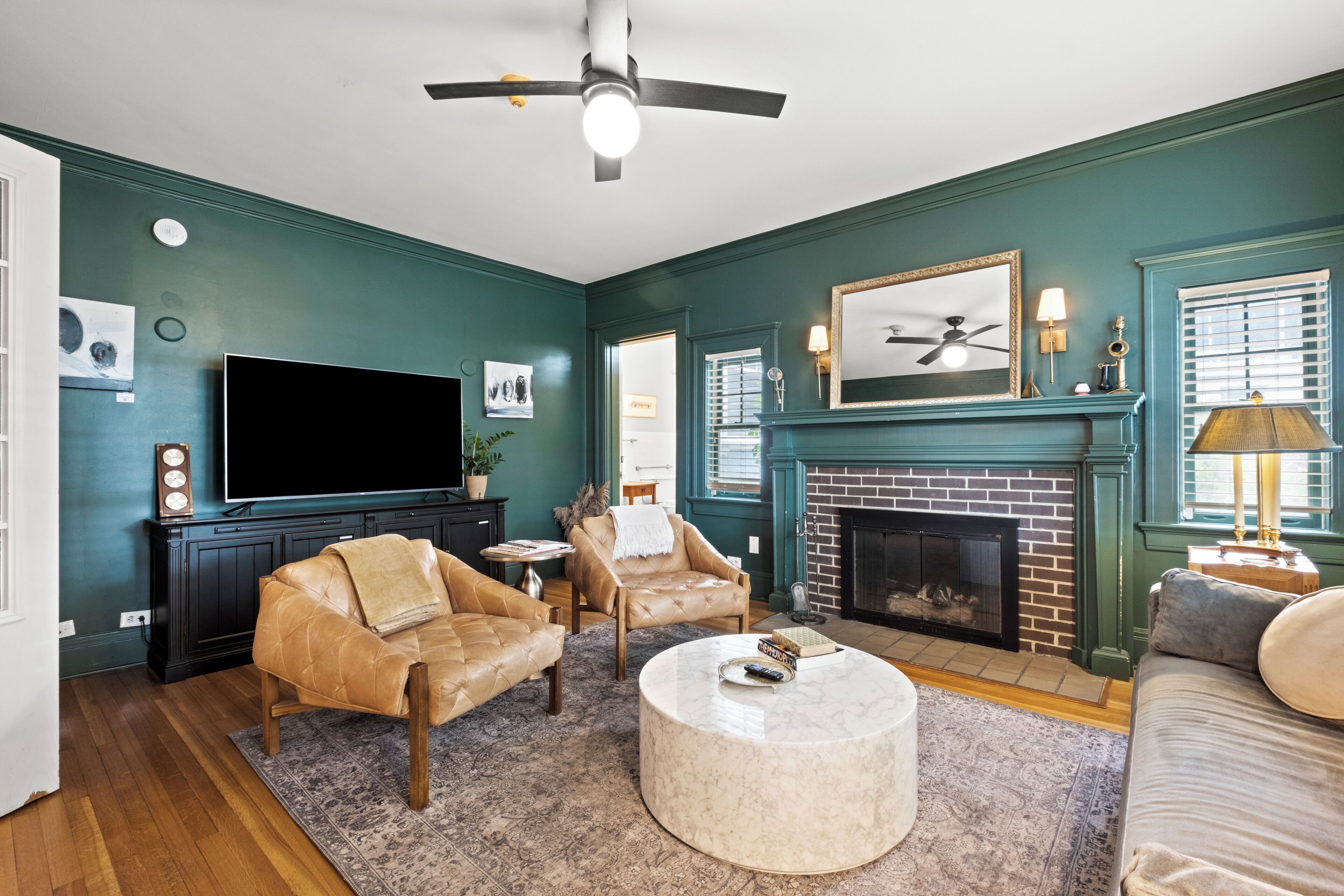 A living room with a TV, leather chairs, a fireplace, and a ceiling fan.