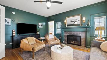 A living room with a TV, leather chairs, a fireplace, and a ceiling fan.