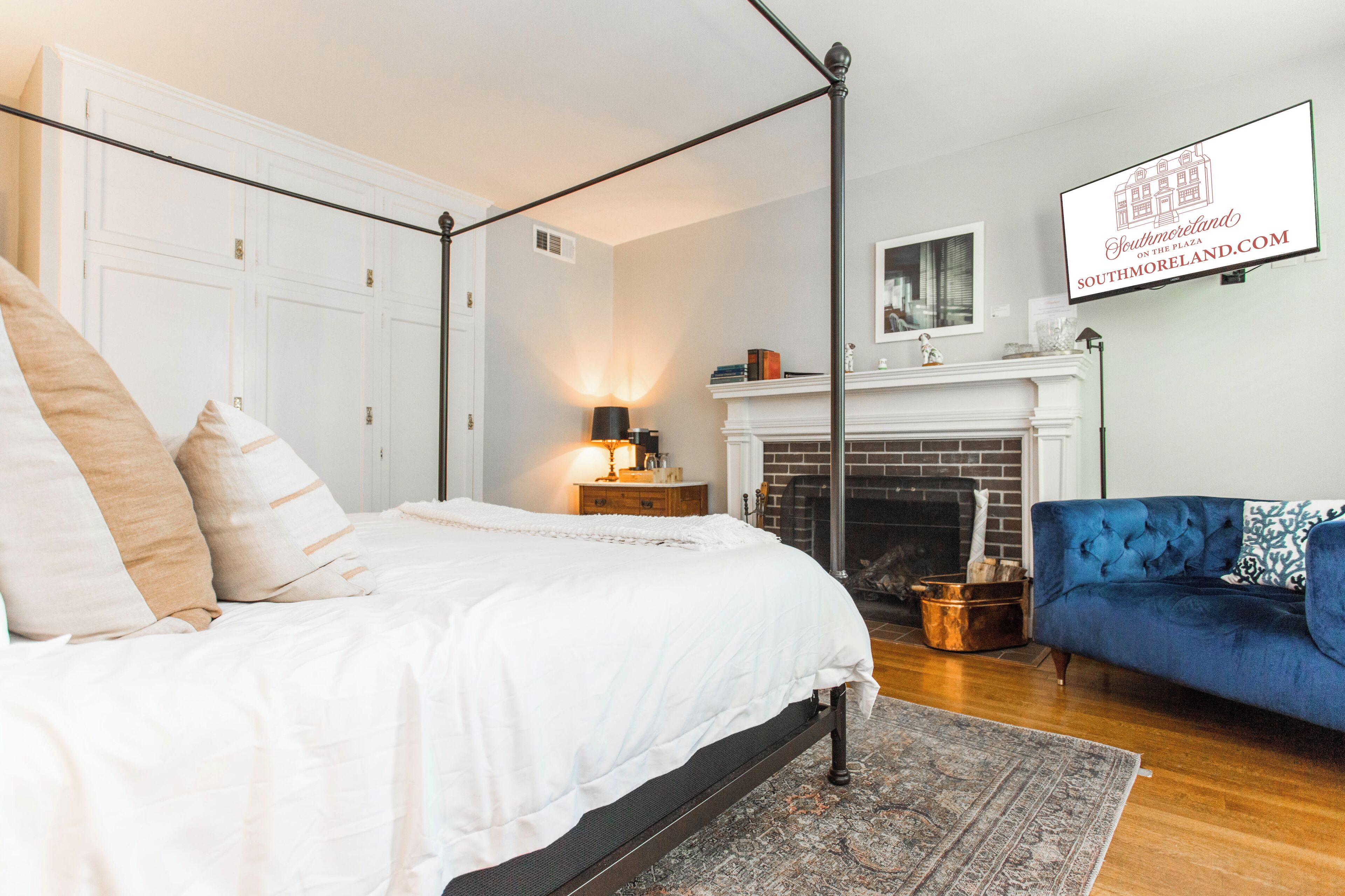 Quarto com cama de dossel, sofá azul, lareira e TV fixada exibindo um site.