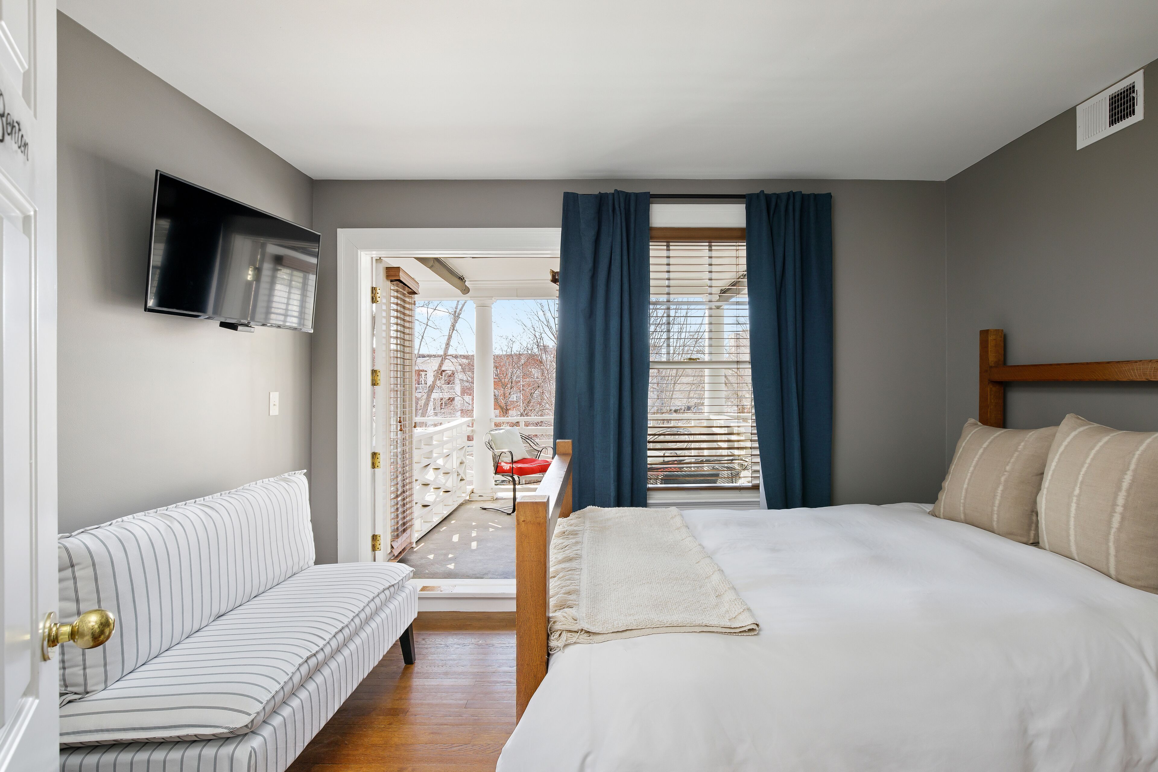 Un dormitorio con cama, sof á, televisión y balcón con una silla.