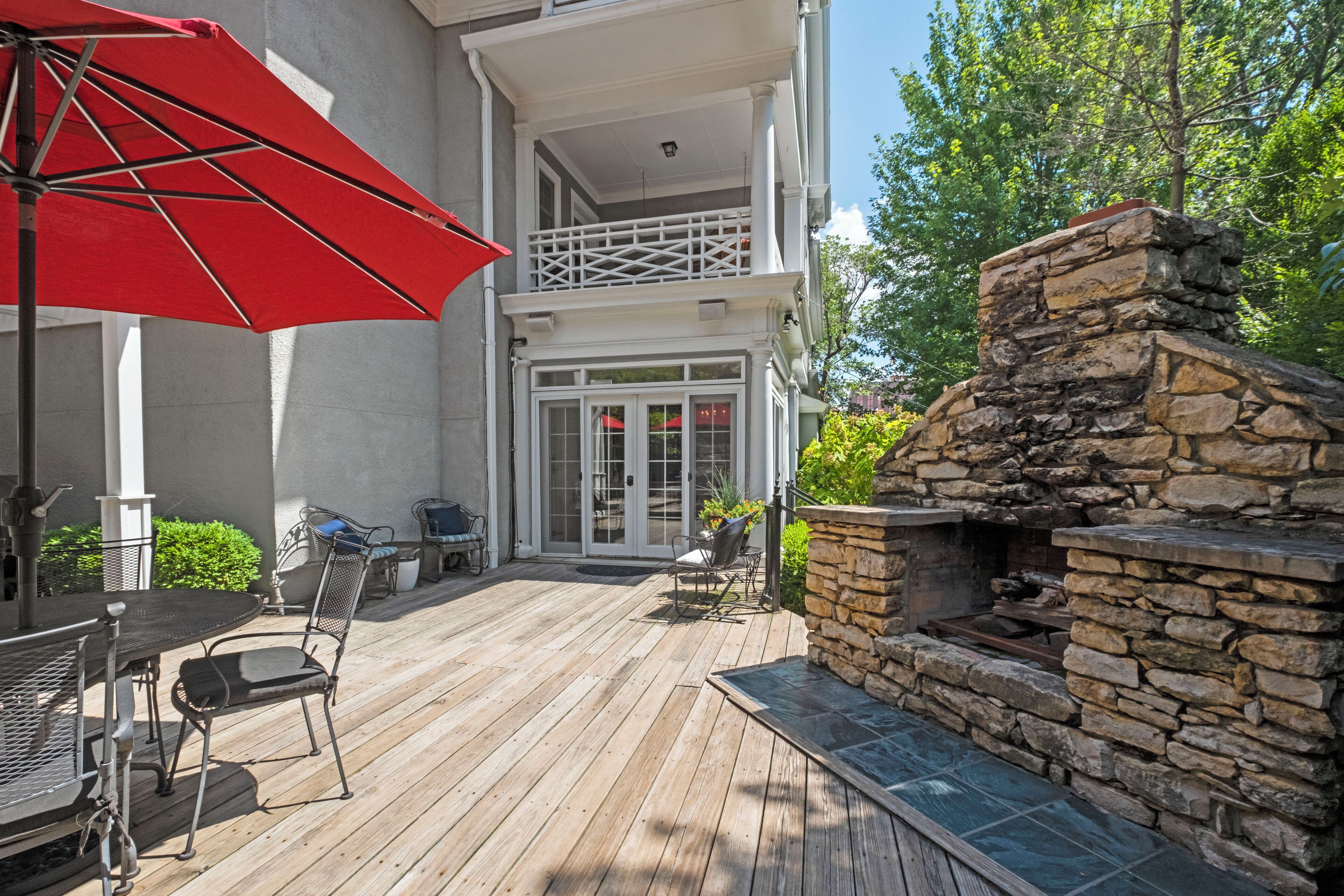 A wooden deck with outdoor furniture, a stone fireplace, and a red umbrella.