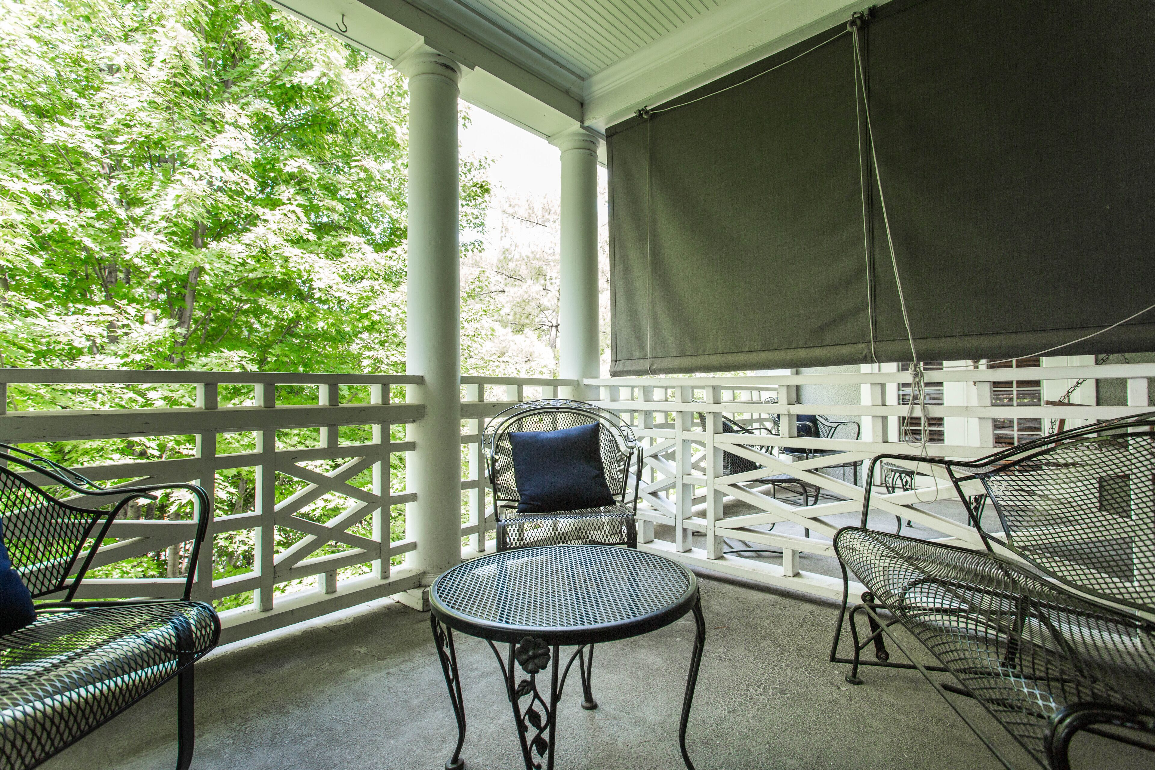 Een overdekt terras met metalen stoelen en een tafel, omringd door witte hekken en begroeiing.