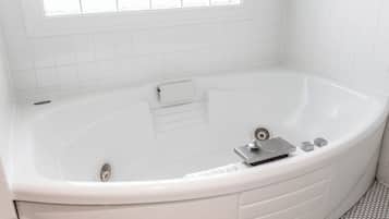 A white bathtub with a control panel, a window above it, and a tiled floor.