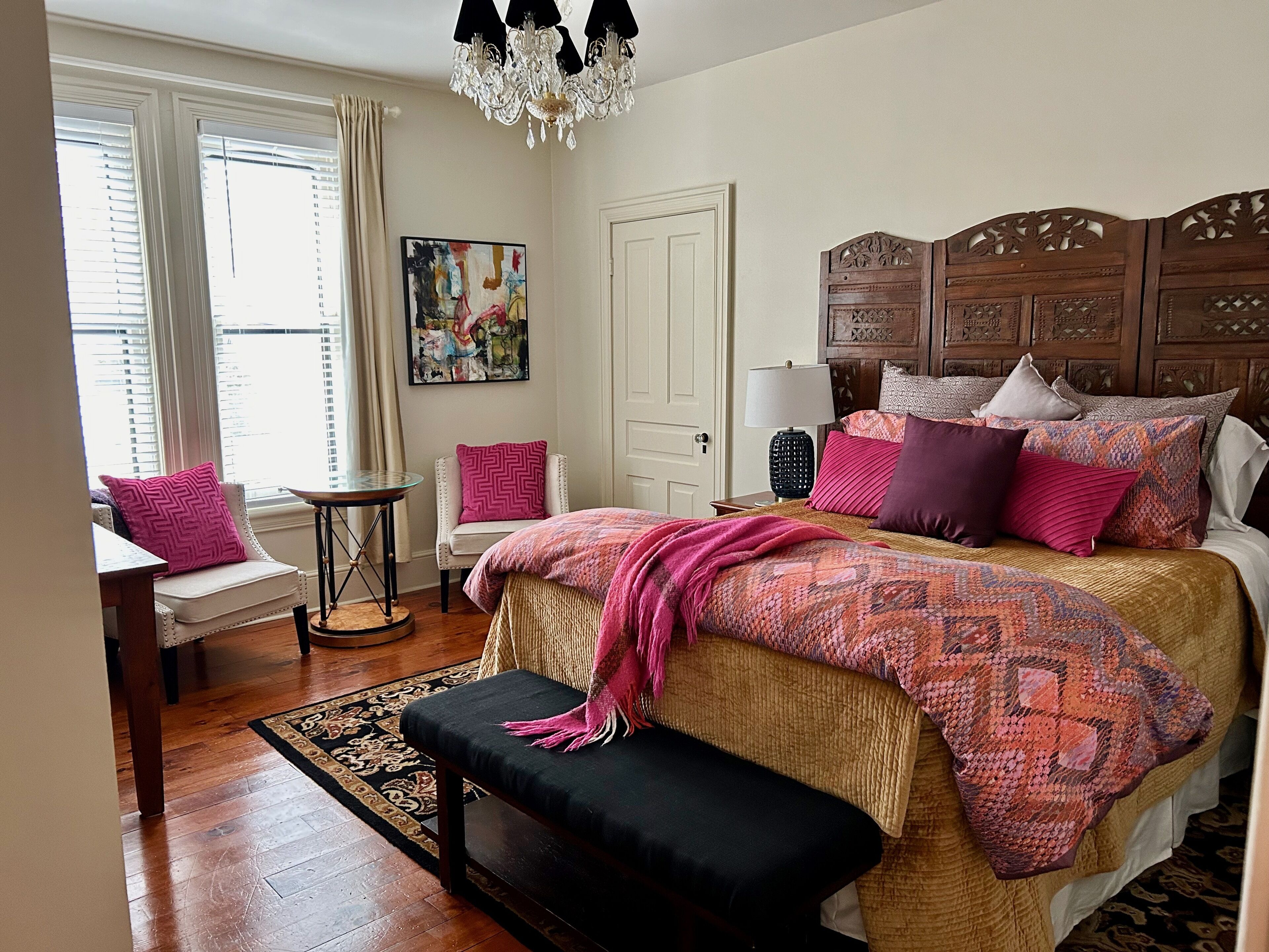 Quarto com uma cama grande, cabeceira de madeira, mesa de cabeceira com abajur, uma cadeira e um quadro na parede.