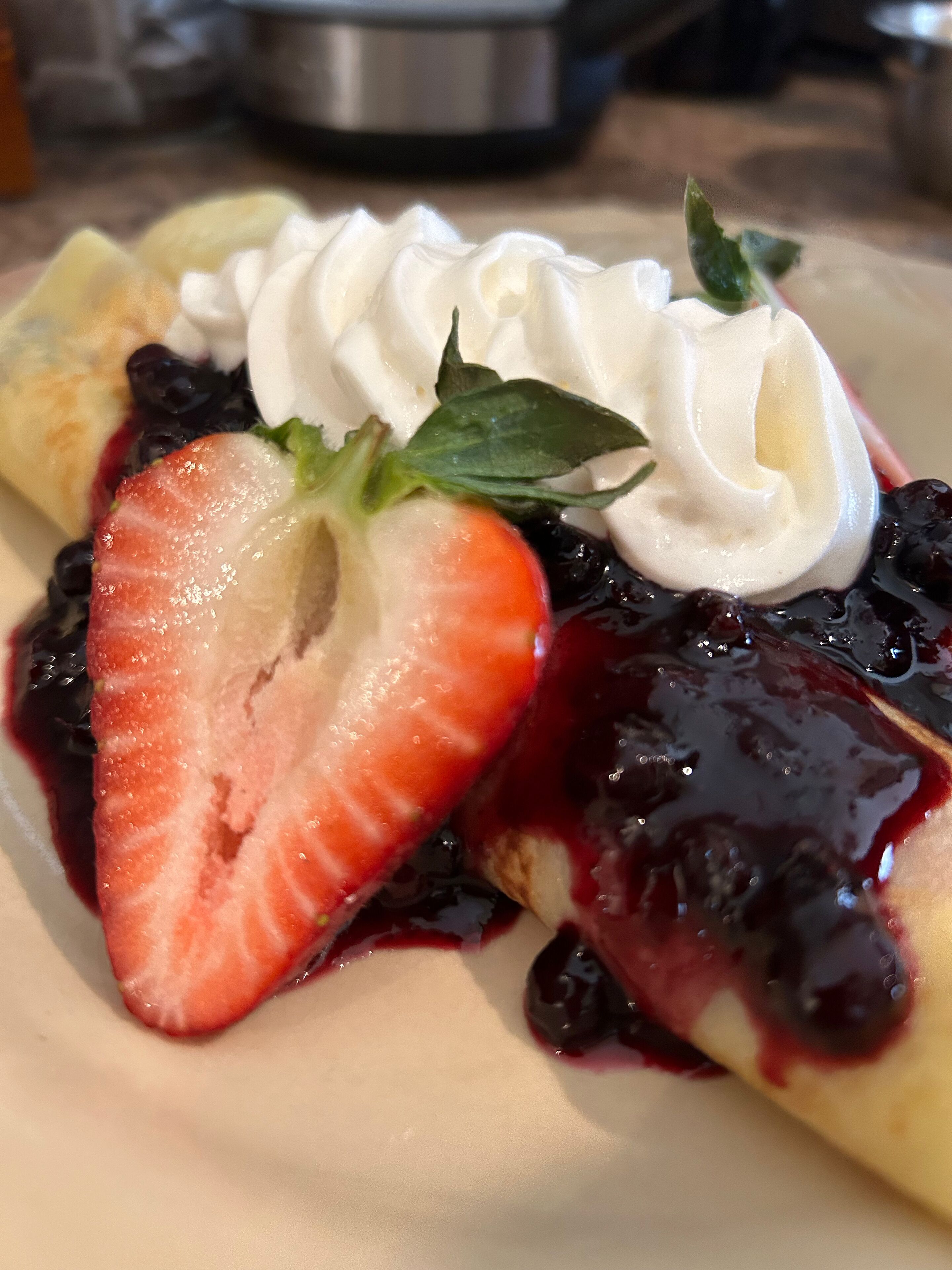 A dessert plate with a crepe, whipped cream, a strawberry, and blueberry sauce.