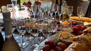 Uma mesa de jantar posta com taças de vinho, garrafas e diversos tipos de comida.
