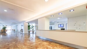 Un'ampia hall con pavimento in marmo, una reception, un televisore e un orologio a parete.