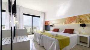 Una camera d'albergo con un letto, una scrivania e una sedia. C'è un'ampia finestra con tende, un quadro appeso al muro e vista sul mare.