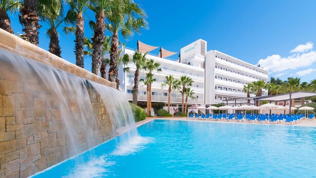 Un albergo con piscina, palme e una cascata.