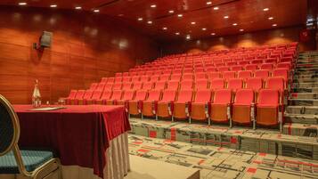 A conference room with rows of red chairs, a table with a red tablecloth, and a patterned carpet.