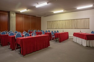 Uma sala de conferências com várias mesas e cadeiras, equipada com garrafas de água e placas de identificação.