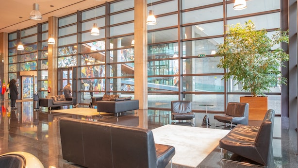 Un vestíbulo amplio con ventanas grandes, asientos modernos y una planta central.