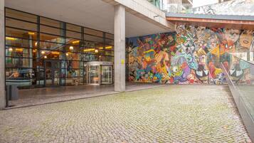 Fachada de hotel con un mural de mosaico, adoquinado y puerta de cristal.