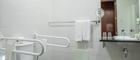 Un baño moderno con inodoro blanco, barras de apoyo, lavamanos con espejo y zona de ducha.