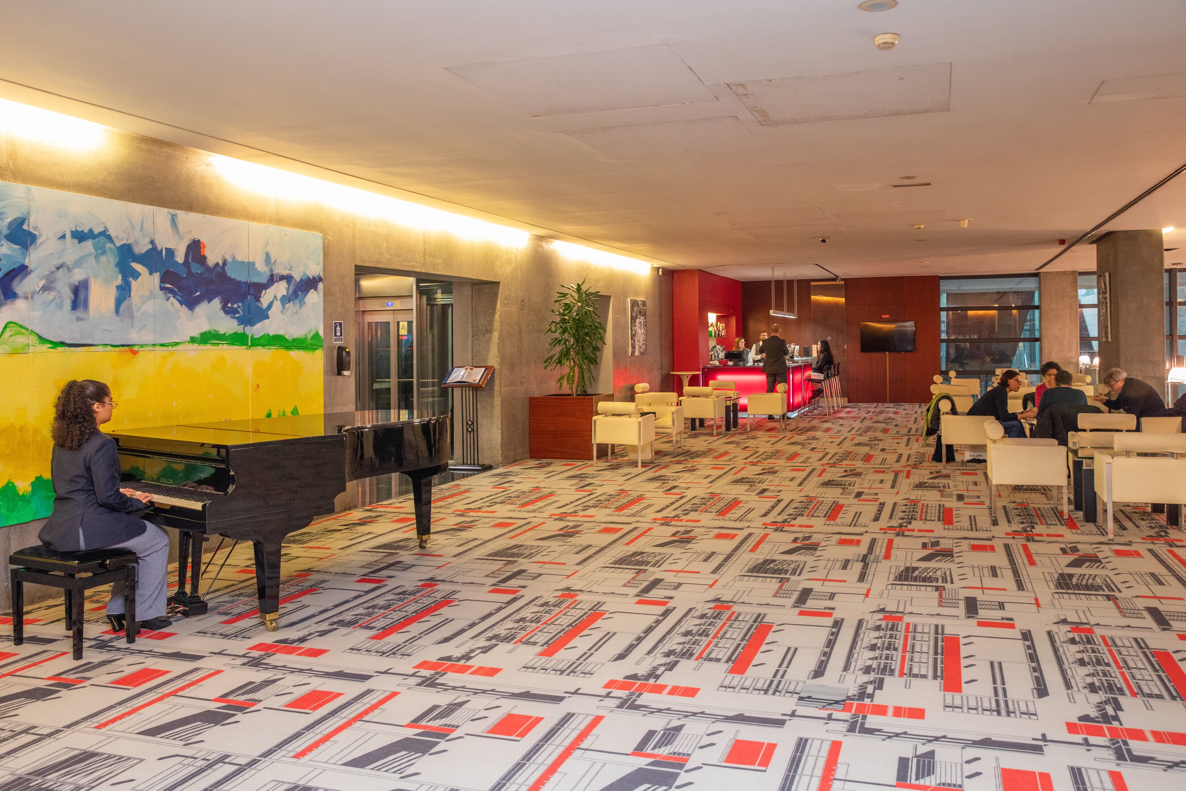 Un vestíbulo con un piano de cola, una recepción y una alfombra estampada.