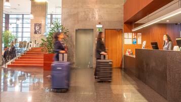 A modern lobby with a reception desk, a staircase, and a large plant.