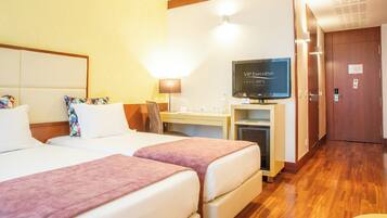 A hotel room with two beds, a desk with a computer, a TV, and a wooden floor.