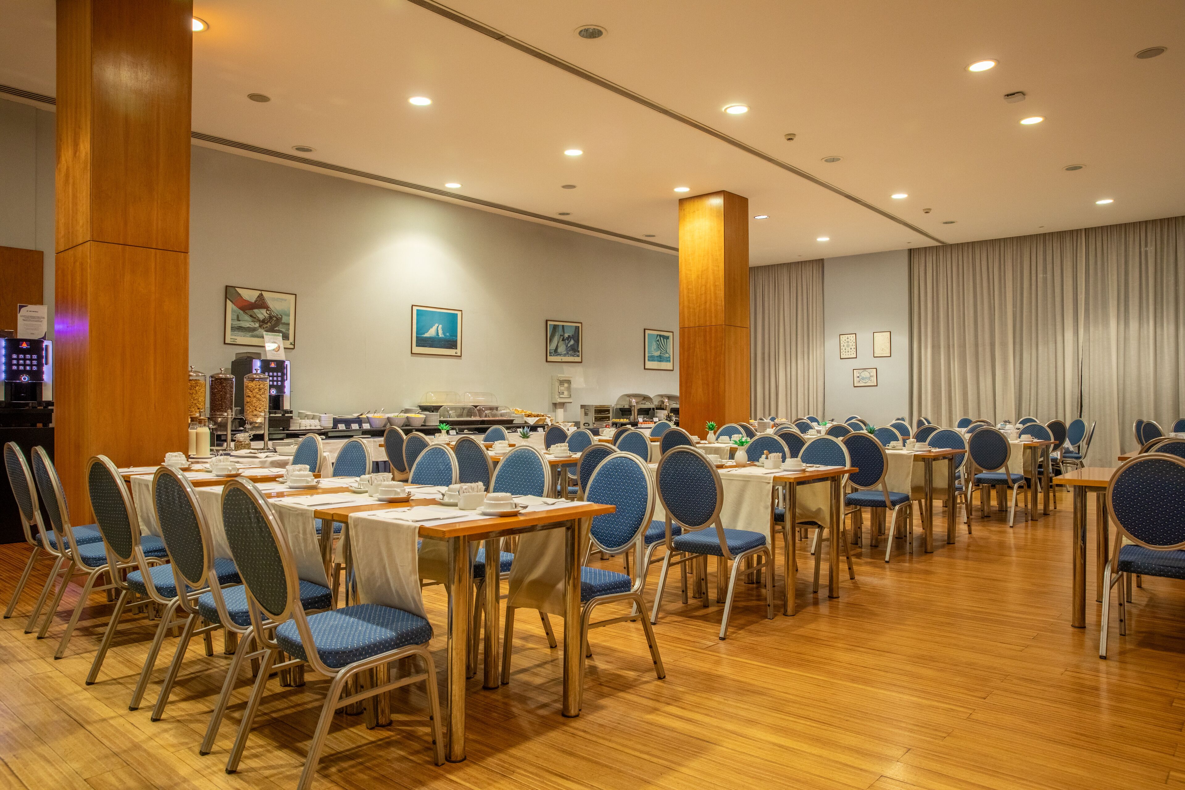 A conference room with multiple tables and chairs, equipped with coffee machines and a buffet area.