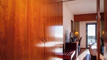 Quarto de hotel com guarda-roupa de madeira, secretária com computador, uma cadeira e uma cama.