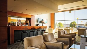 A modern hotel lobby with a bar area, comfortable seating, and large windows offering a view of the outside. - VIP Executive Santa Iria Hotel (Loures)