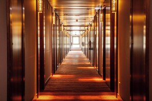 Un long couloir étroit, avec des portes de chaque côté, qui mène à une sortie lumineuse au bout.