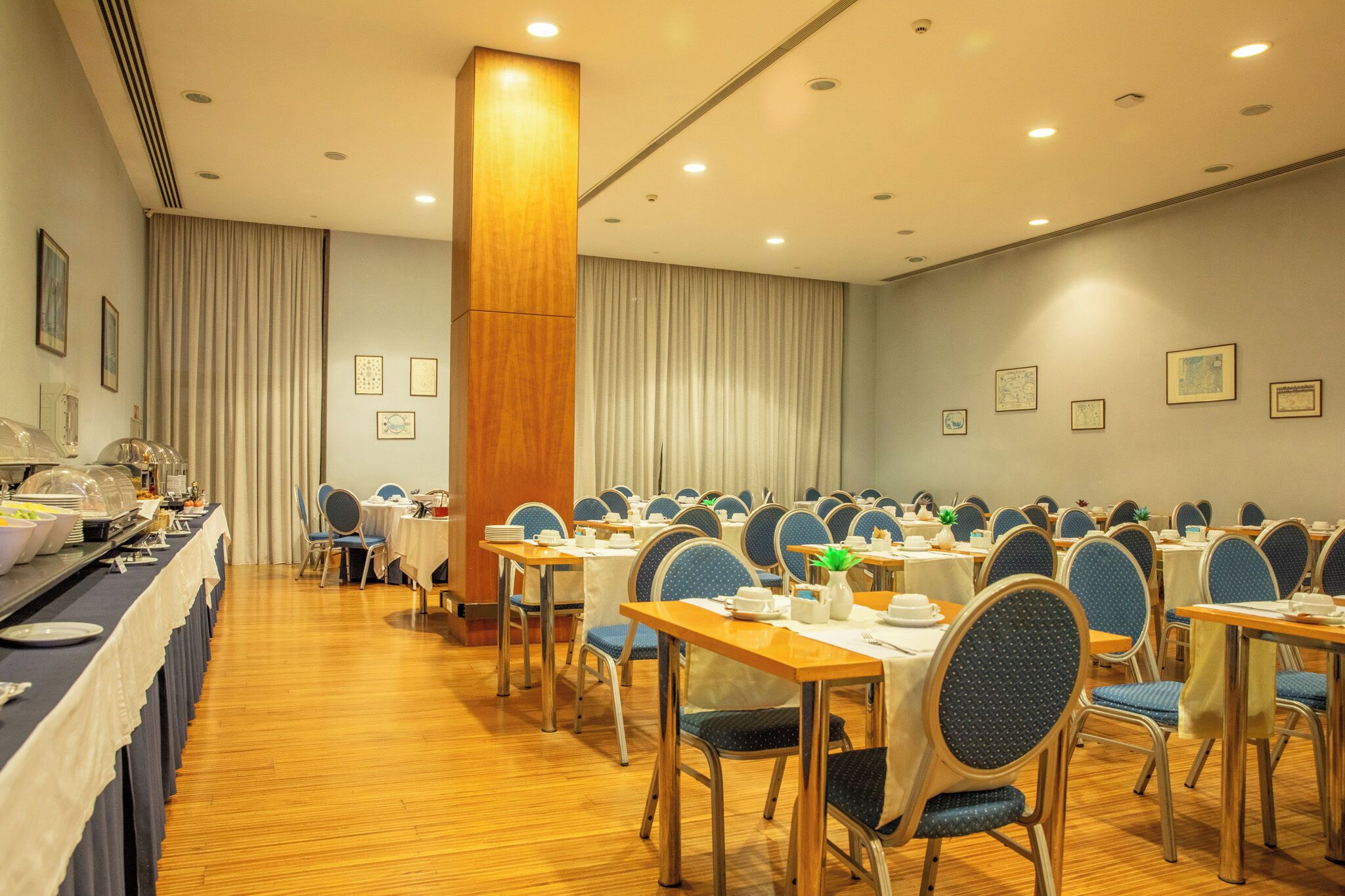 A conference room with multiple tables and chairs, a buffet area on the left, and a large wooden pillar.