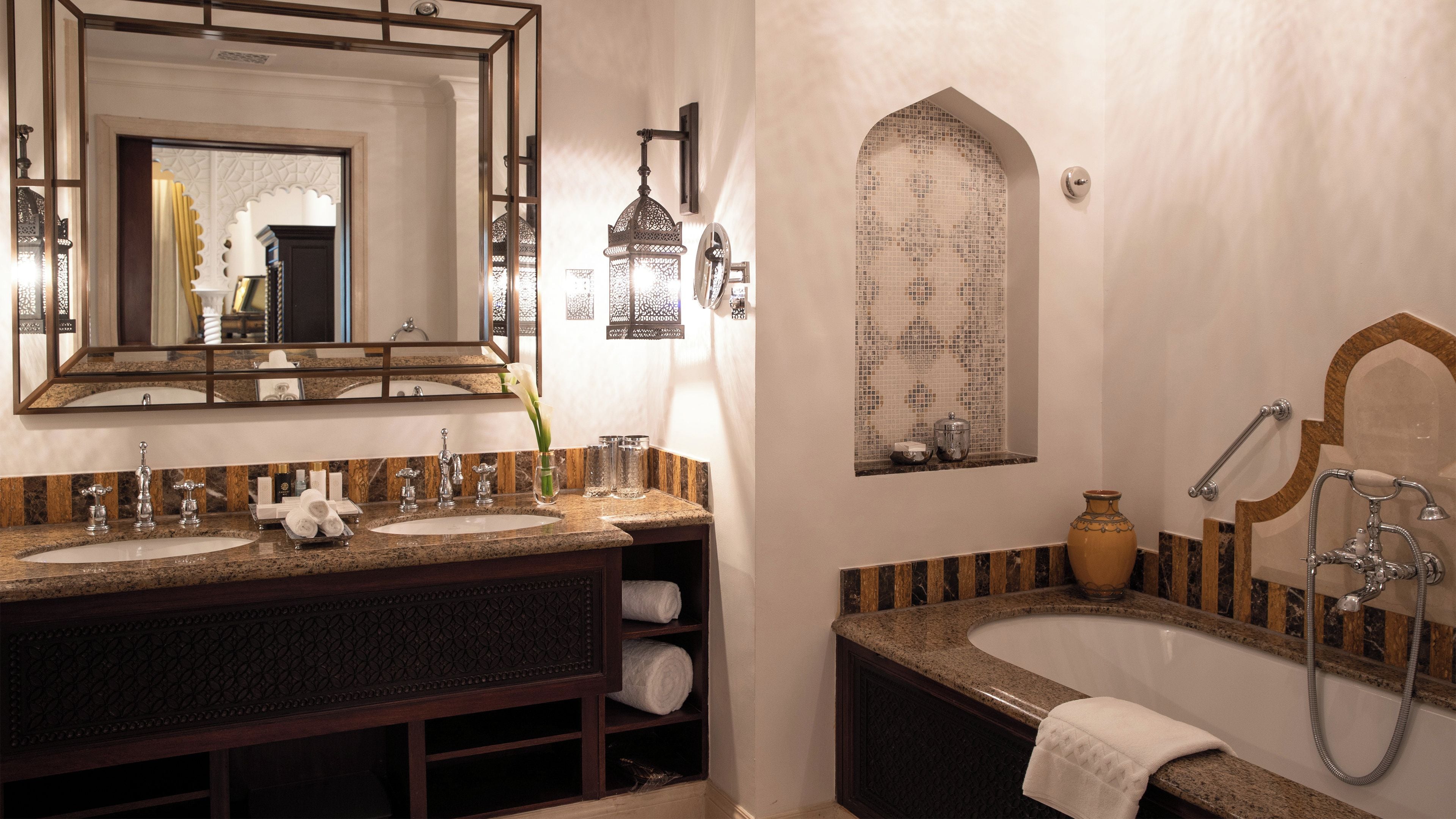 Un baño con dos lavamanos, un espejo grande, una bañera con ducha y azulejos decorativos.